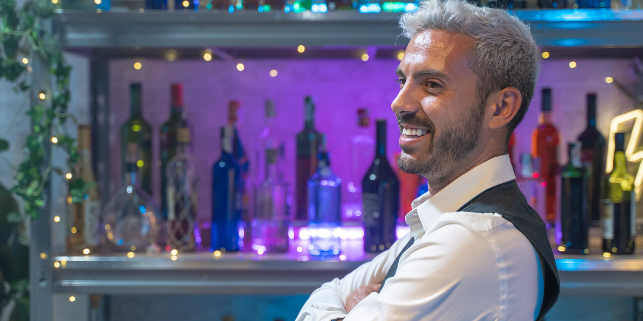 Barman portrait in a white shirt and black apron smiling at nightclub. High quality photo