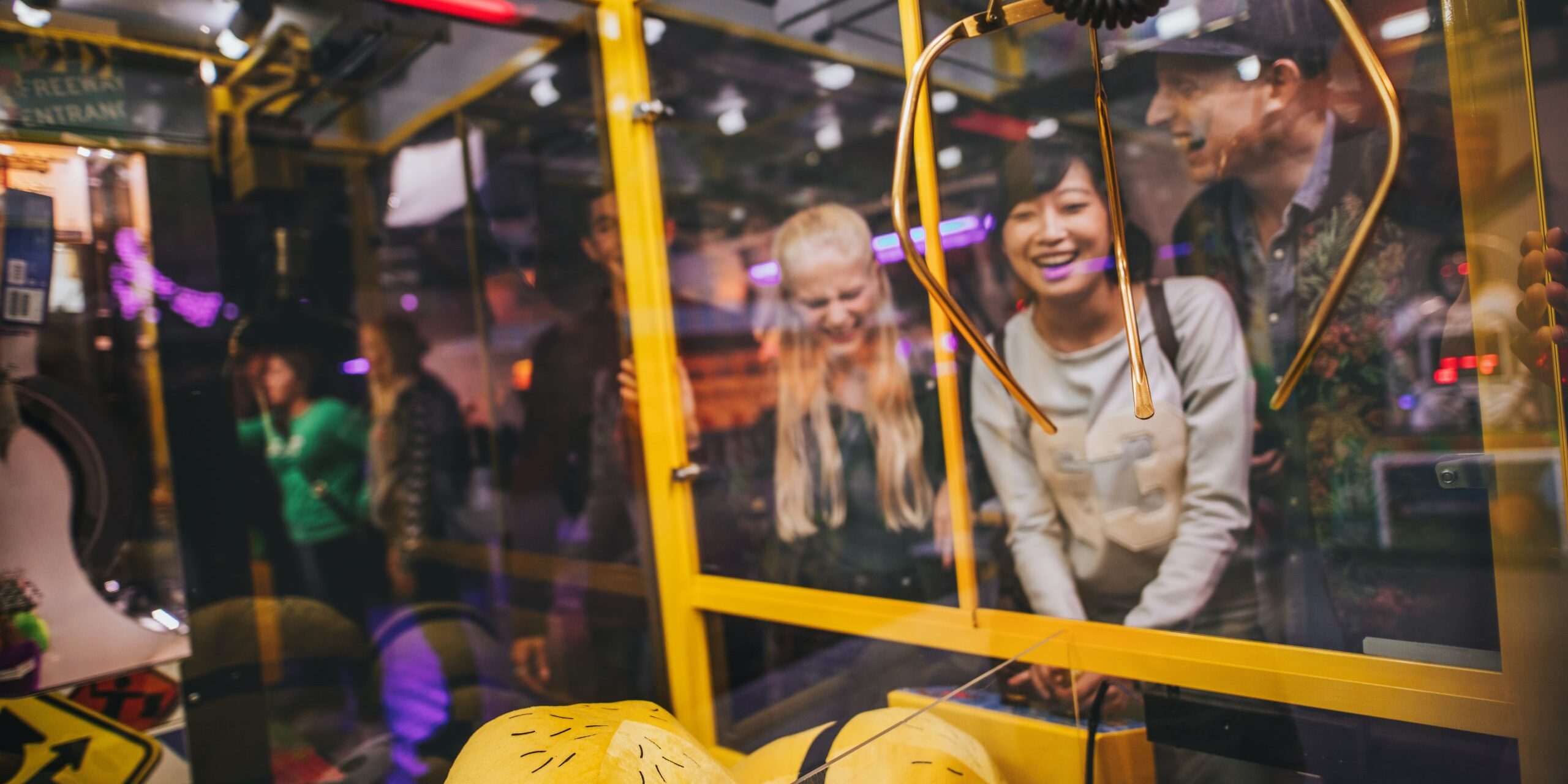 Happy young woman playing toy grabbing game with friends at amusement park.